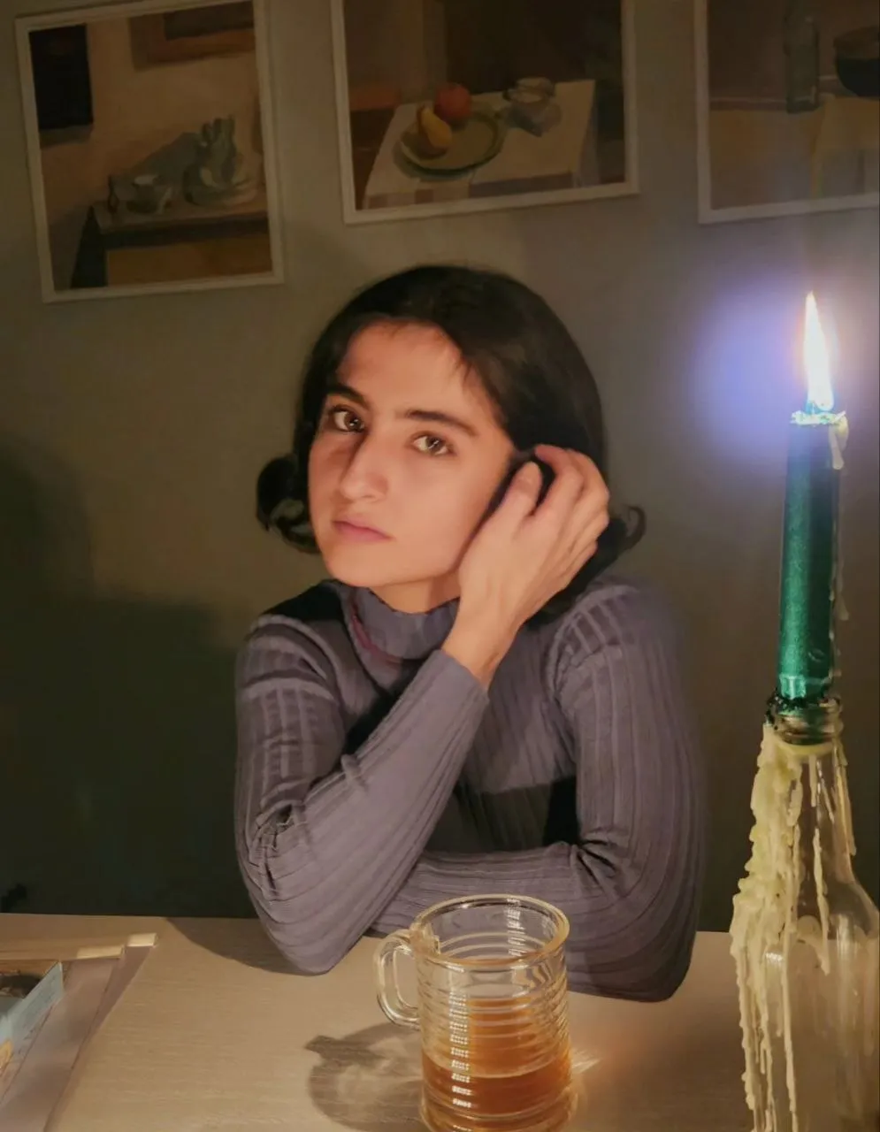 Faezeh Hamd working on a canvas at her desk, lit by a lamp in her studio